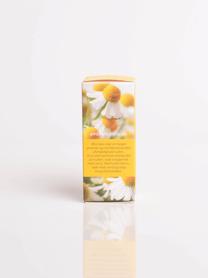 Gelbe Verpackung für ätherisches Öl mit Kamillenblüten auf weißer, reflektierender Oberfläche