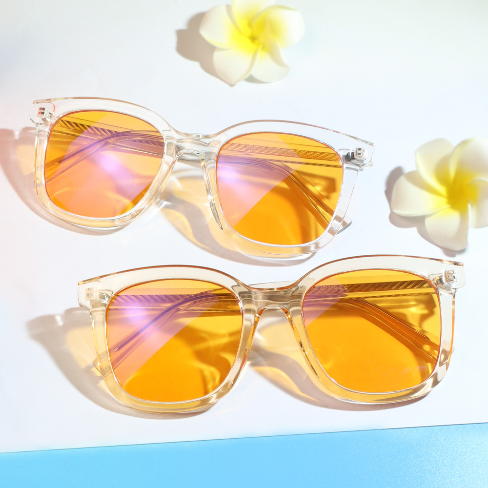 Zwei transparente Sonnenbrillen mit orange-violetten Spiegelgläsern und Plumeria-Blüten vor weißem Hintergrund