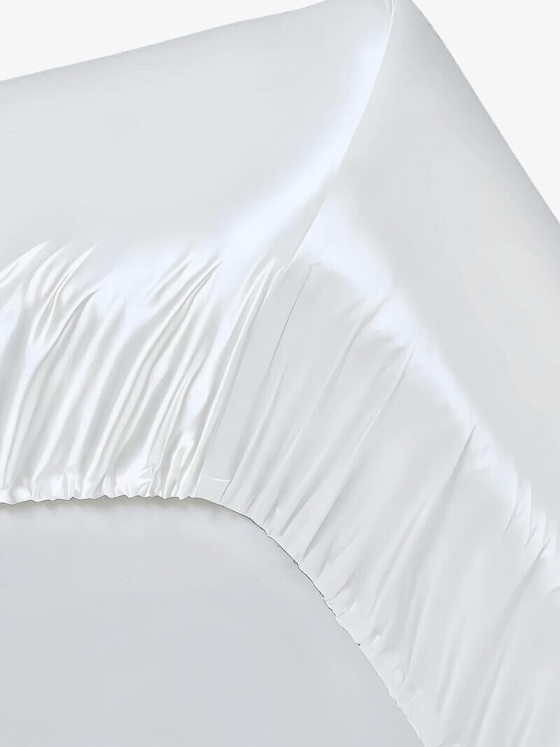 Ecke eines weißen Satin-Spannbettlakens mit Gummizug und glänzendem Faltenwurf