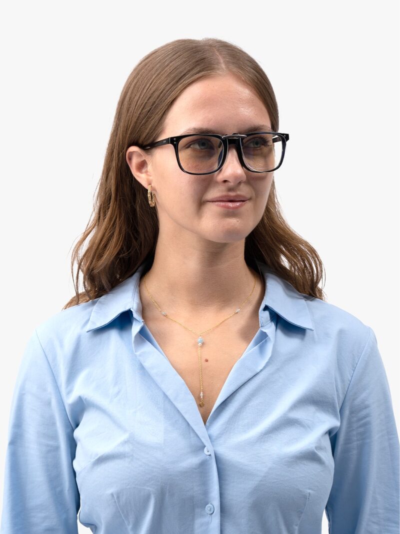 Frau mit schwarzer Brillenfassung und hellblauem Hemd, dazu goldene Y-Kette und kleine goldene Creolen