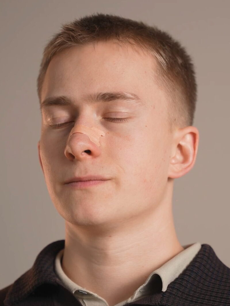 Junger Mann mit Nasenstrip auf dem Nasenrücken, geschlossene Augen und entspannter Gesichtsausdruck