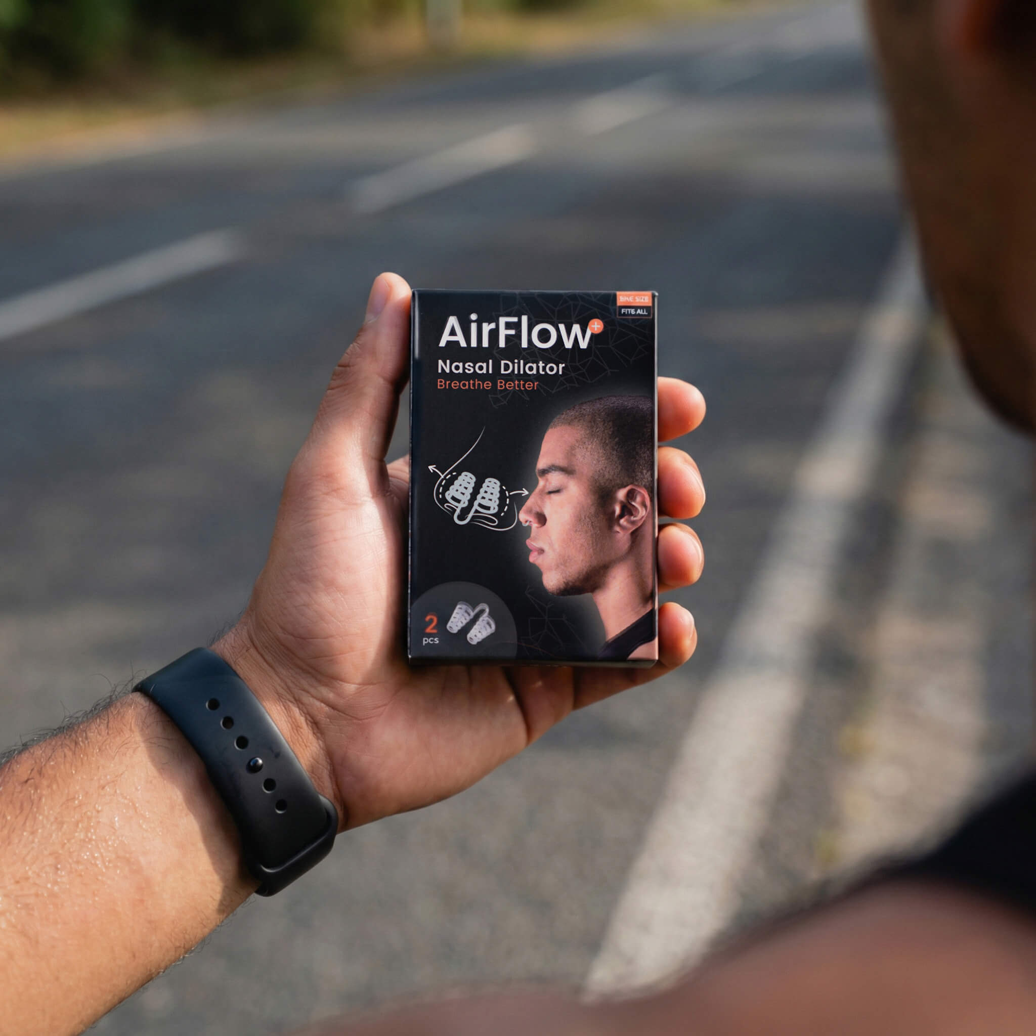 Hand mit Smartwatch hält eine Packung AirFlow Nasendilatator vor unscharfem Straßenhintergrund