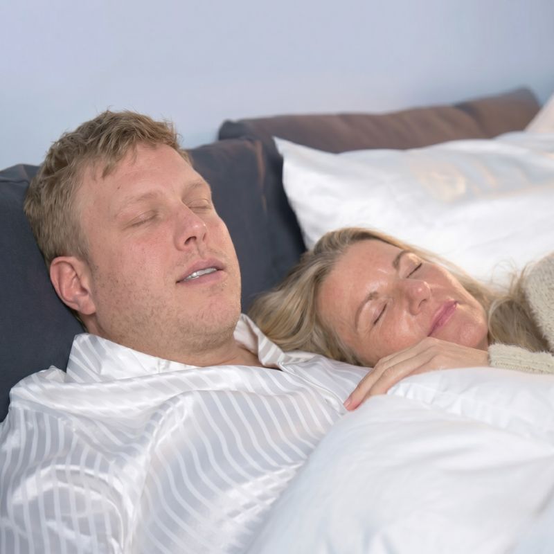 Schnarchschutz: entspanntes Paar schläft nebeneinander im Bett unter weißer Decke